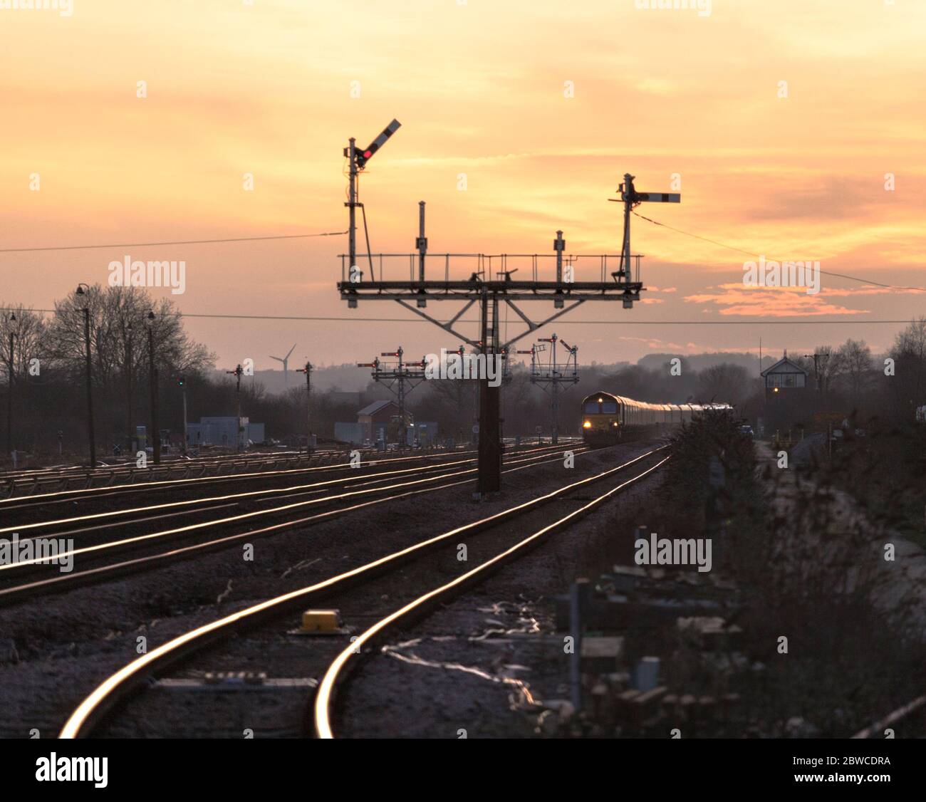 DB Cargo Rail locomotiva UK classe 66 che trasporta un treno merci che passa il segnale della grande staffa del semaforo a Barnetby, Lincs, al tramonto Foto Stock