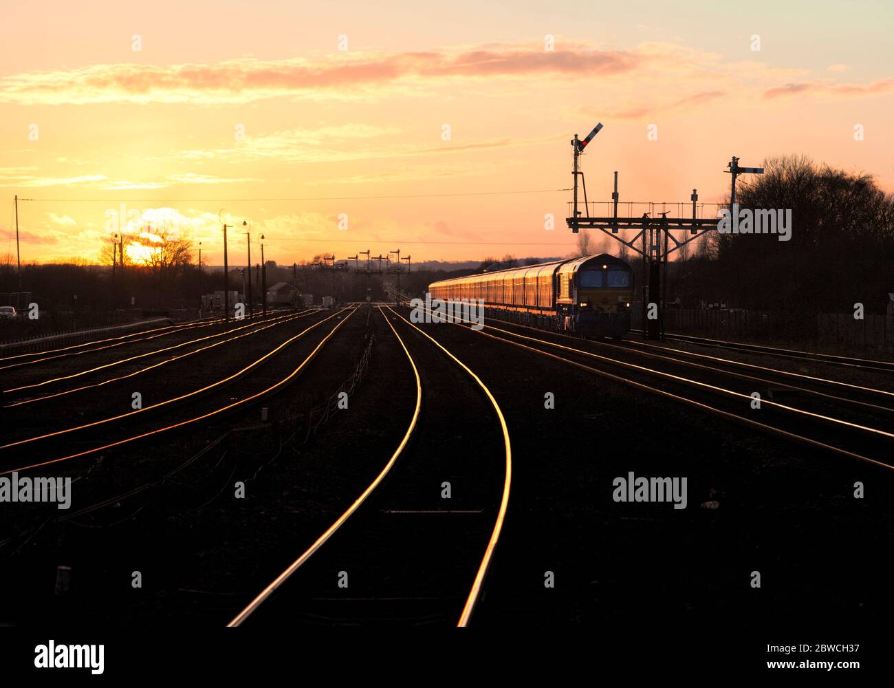 DB CARGO Rail classe 66 locomotiva 66105 che passa il segnale della grande staffa del semaforo a Barnetby, Lincs, che si intravita al tramonto con carri a biomassa. Foto Stock