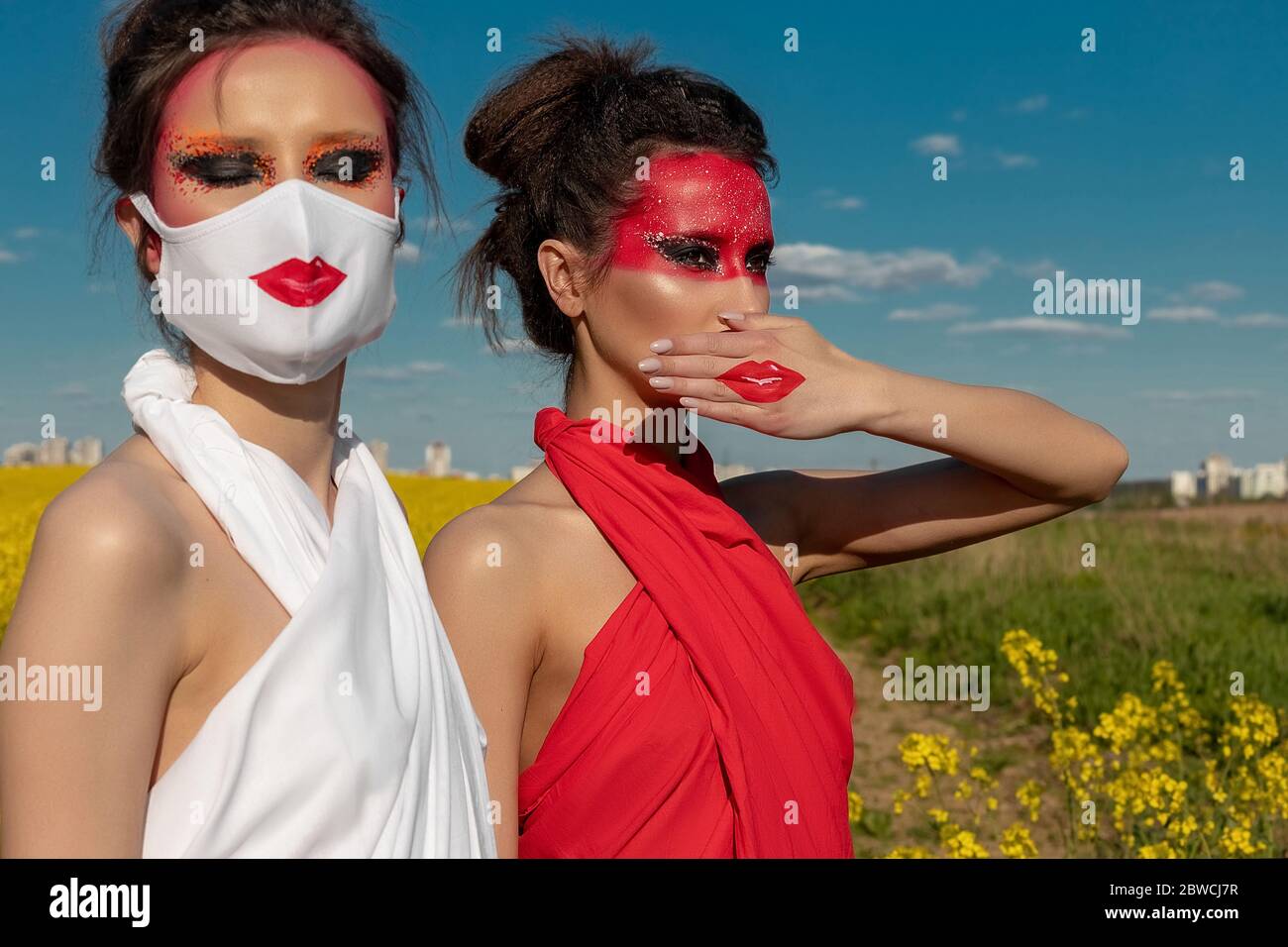 Due belle ragazze di brunette con trucco creativo luminoso in tunics contro un cielo blu. Una ragazza in una maschera, l'altra ragazza chiude la bocca con Foto Stock