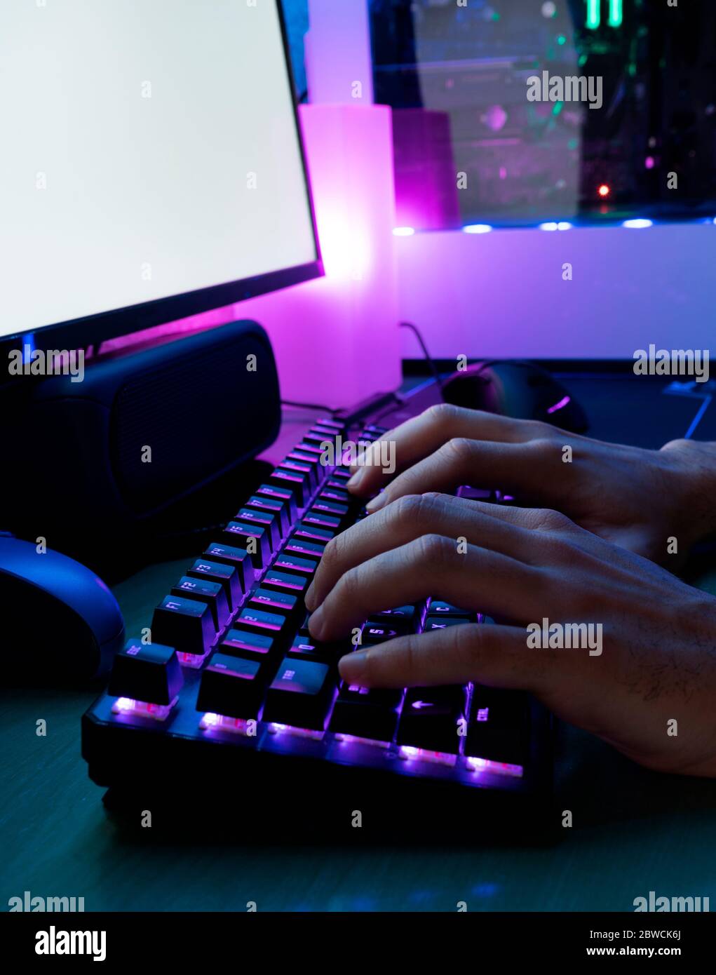 Immagine della digitazione delle mani dell'uomo. Mani di un giocatore su una tastiera. Lo sfondo è illuminato con luci LED. Foto Stock