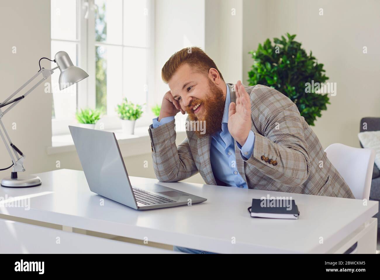 Videochiamata con chat online. Uomo d'affari positivo che effettua videochiamata tramite laptop e mano sventolante. Foto Stock