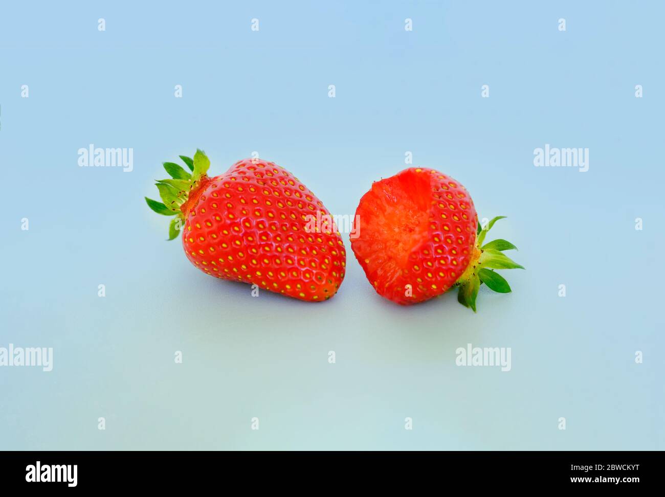 due fragole con foglie di fragola su sfondo grigio. Bacche intere e amarene. Vendita, cucina Foto Stock