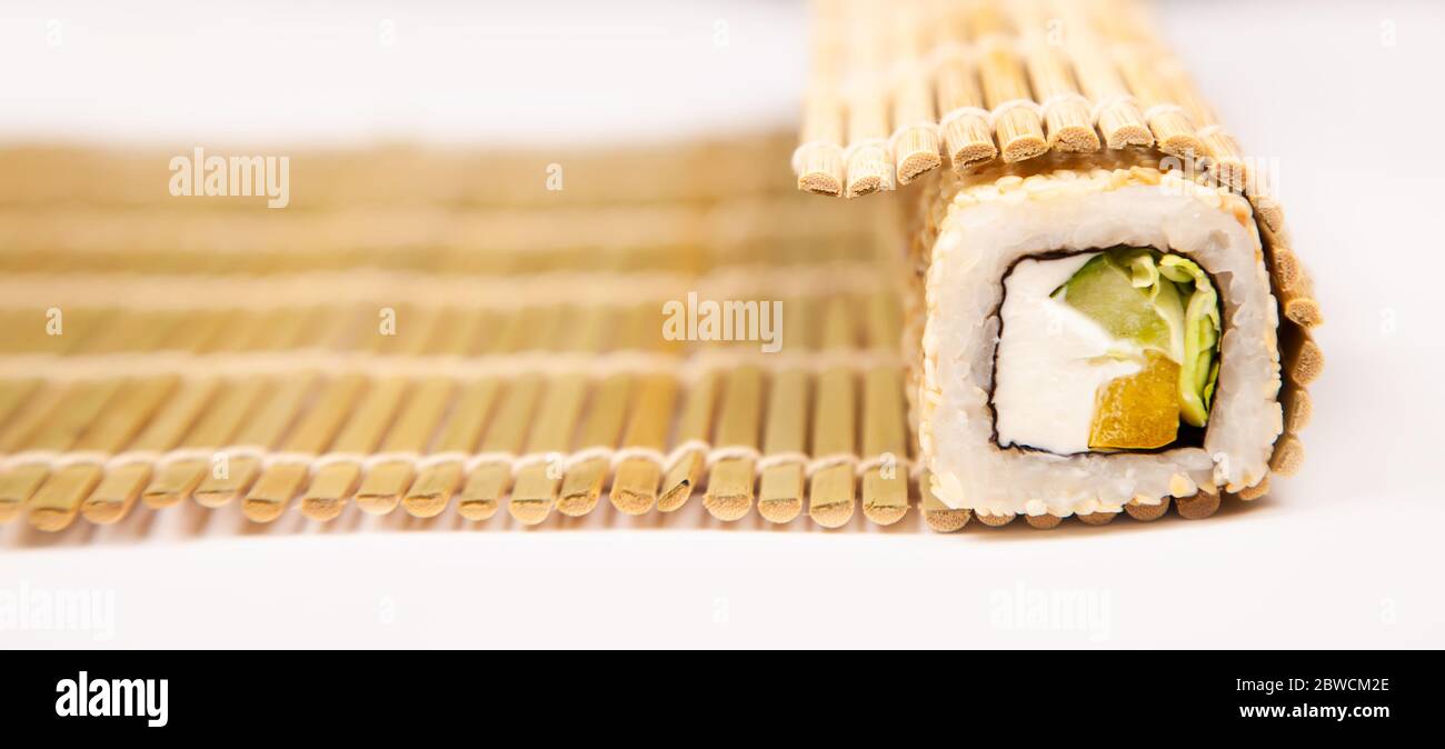 Makishu per la preparazione di sushi e panini con formaggio di pesce e semi di sesamo dalla cucina giapponese, stuoia di bambù con rotolo api su sfondo bianco Foto Stock