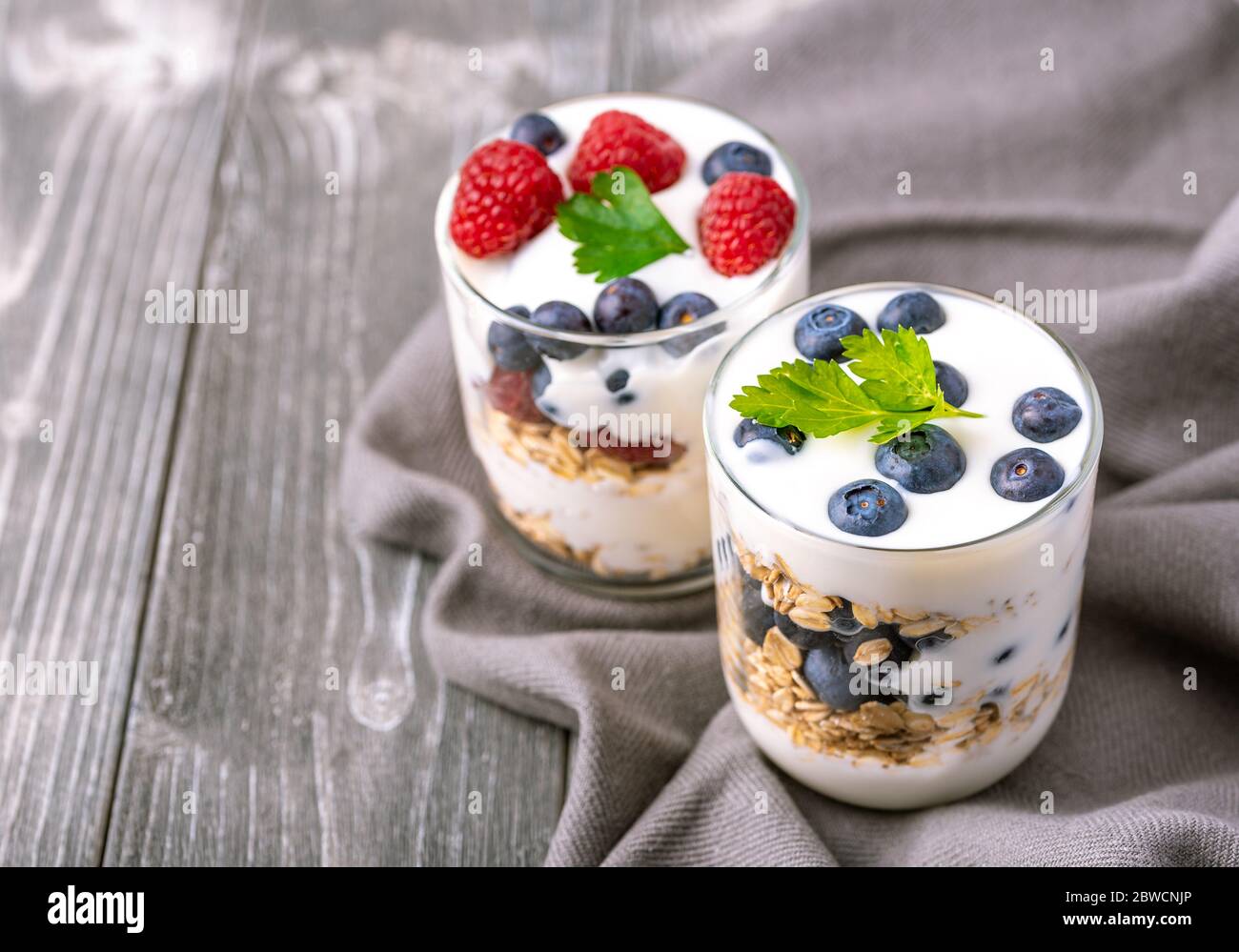 Yogurt bianco in vaso di vetro con mirtilli su sfondo grigio. Foto Stock