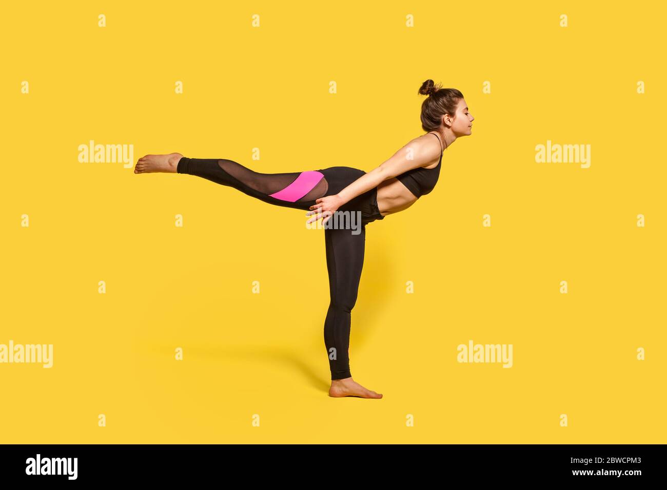 Guerriero 3 posa. Donna sottile con capelli bun in stretto abbigliamento sportivo praticando yoga, facendo Virabhadrasana III esercizio su una gamba, stretching muscoli e bal Foto Stock