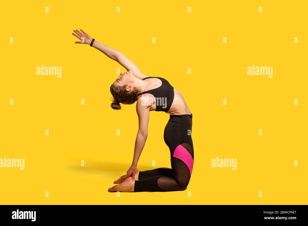 Posa cammello. Donna atletica con peli in tight sportswear pratica yoga, facendo schiena spinale curvando esercizio strucasana con mano sollevata, allunghe Foto Stock