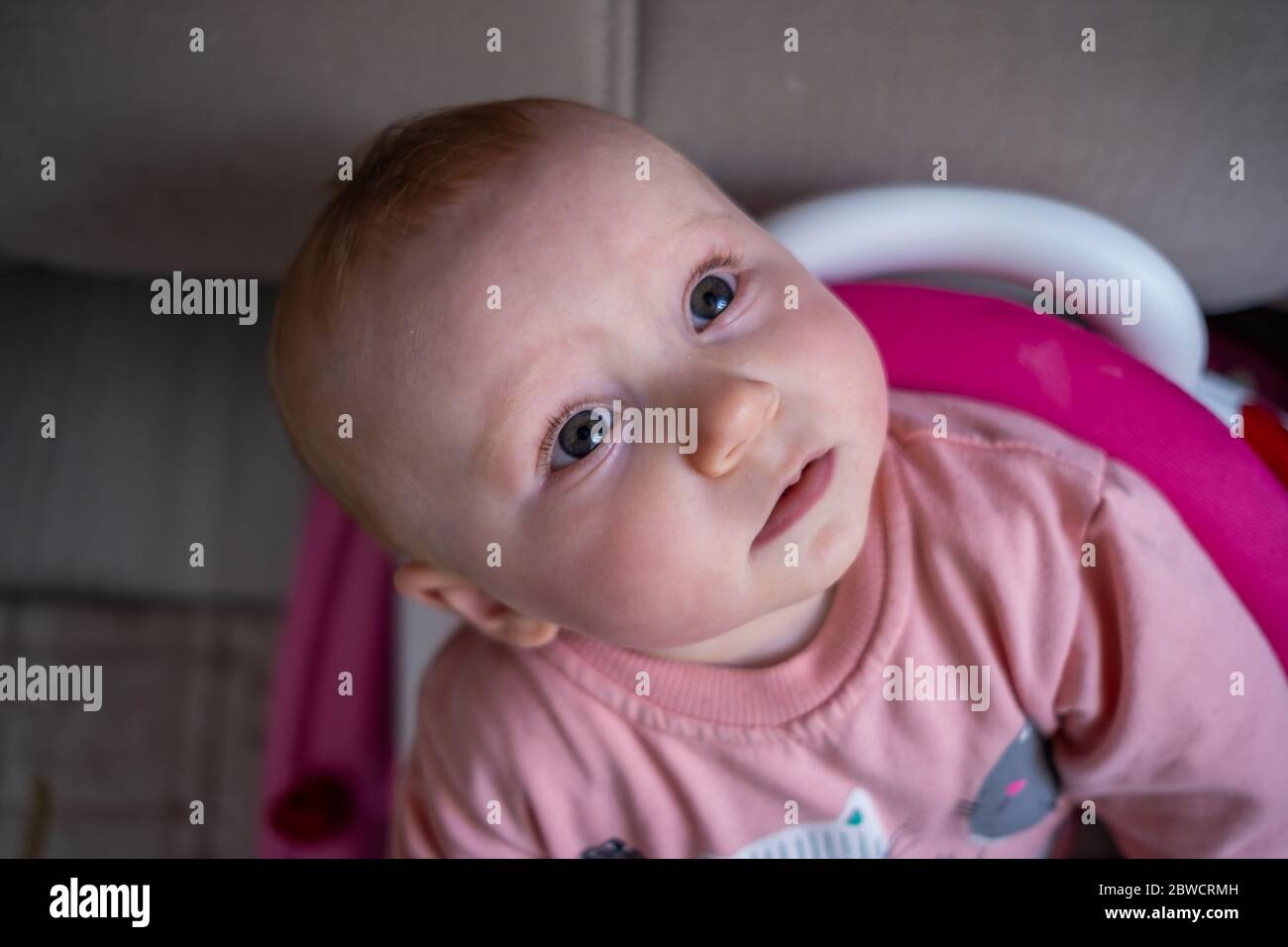 Vista ad alto angolo di cute bionda baby girl guardando fino a macchina fotografica in baby walker Foto Stock