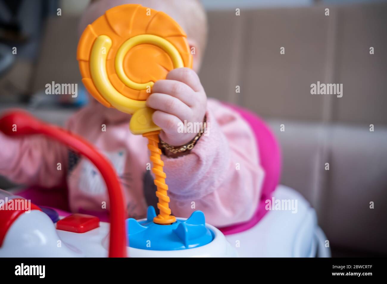 Primo piano di cute bambina che gioca con i giocattoli gialli cerchio in baby walker Foto Stock