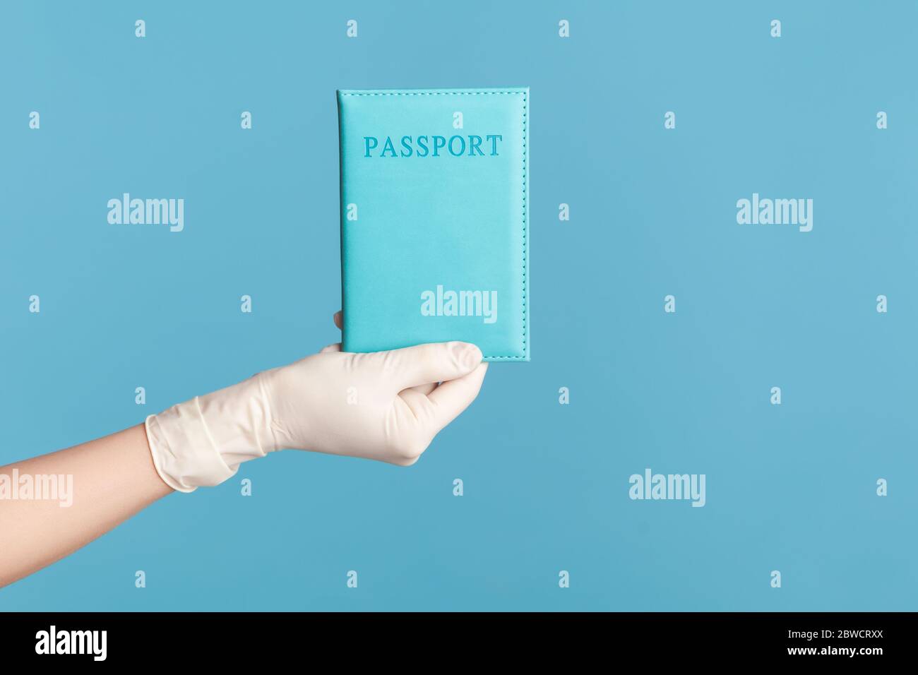 Profilo Vista laterale primo piano della mano umana in guanti chirurgici bianchi che tengono in mano il passaporto. Interno, studio girato, isolato su sfondo blu. Foto Stock
