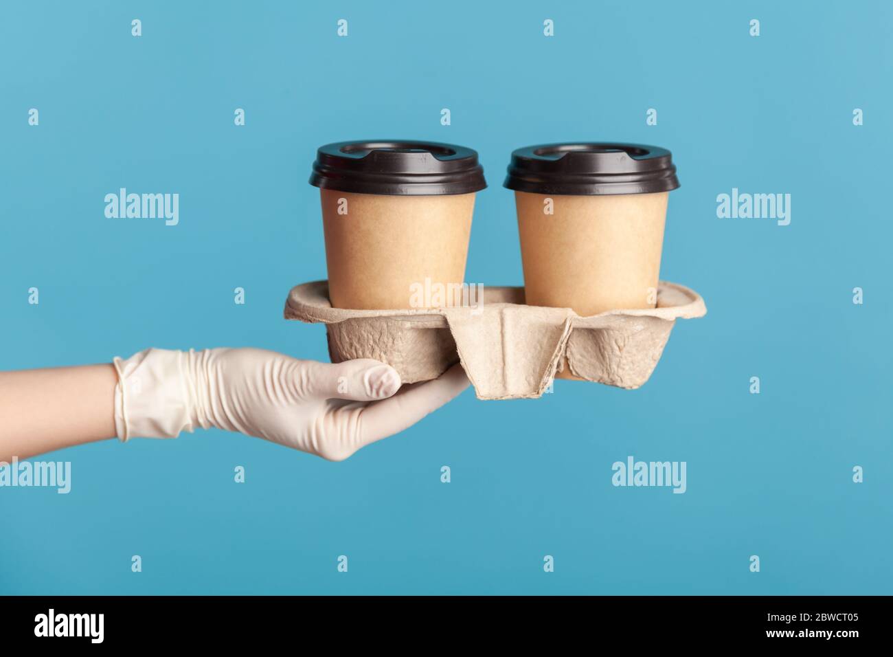 Profilo Vista laterale primo piano della mano umana in guanti chirurgici bianchi che tengono in mano e mostrano una tazza di tazza da takeaway calda. Interno, studio shot, isola Foto Stock