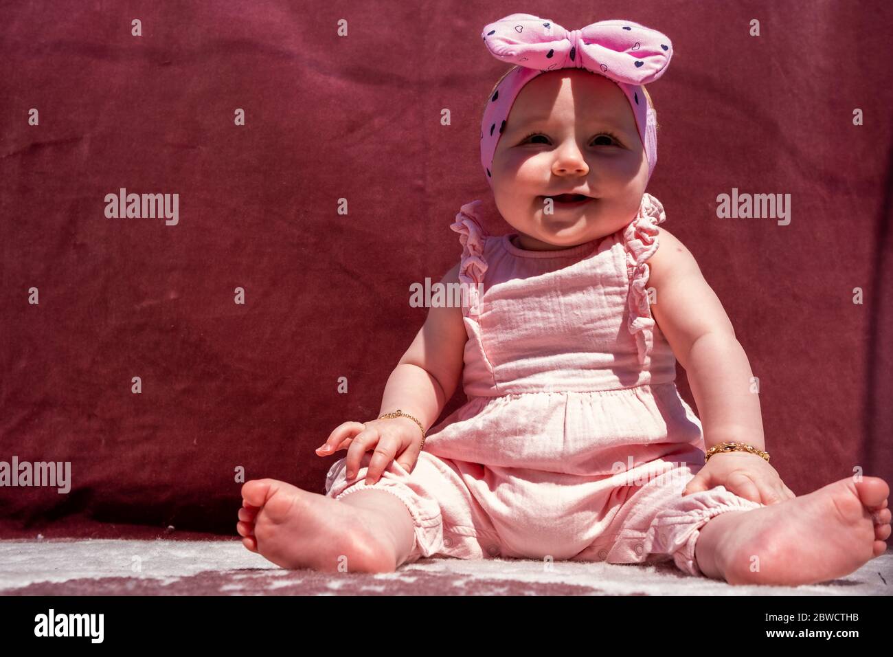 Carina bambina indossa cappello e siediti sul tappeto all'esterno, guardando la macchina fotografica e sorridendo Foto Stock