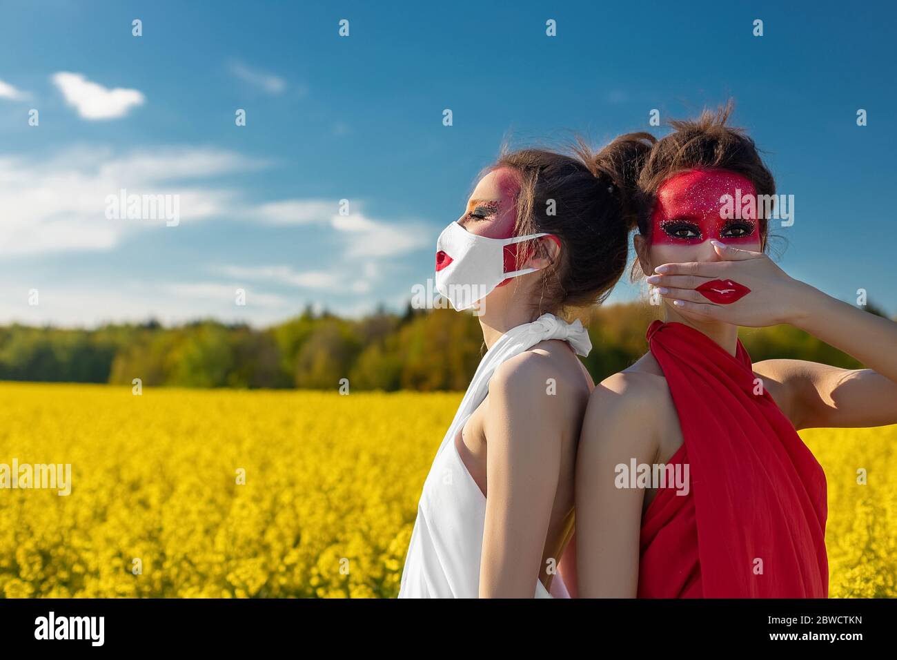 Due belle ragazze di brunette con trucco creativo luminoso in tunics su uno sfondo di un campo di fiori gialli e cielo blu. Una ragazza in una maschera Foto Stock