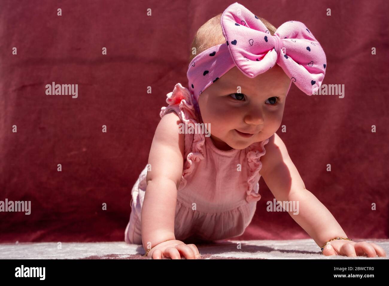 Carina bambina indossare adorabile cappello facendo push-up all'aperto, guardando la fotocamera e sorridendo su sfondo rosso Foto Stock