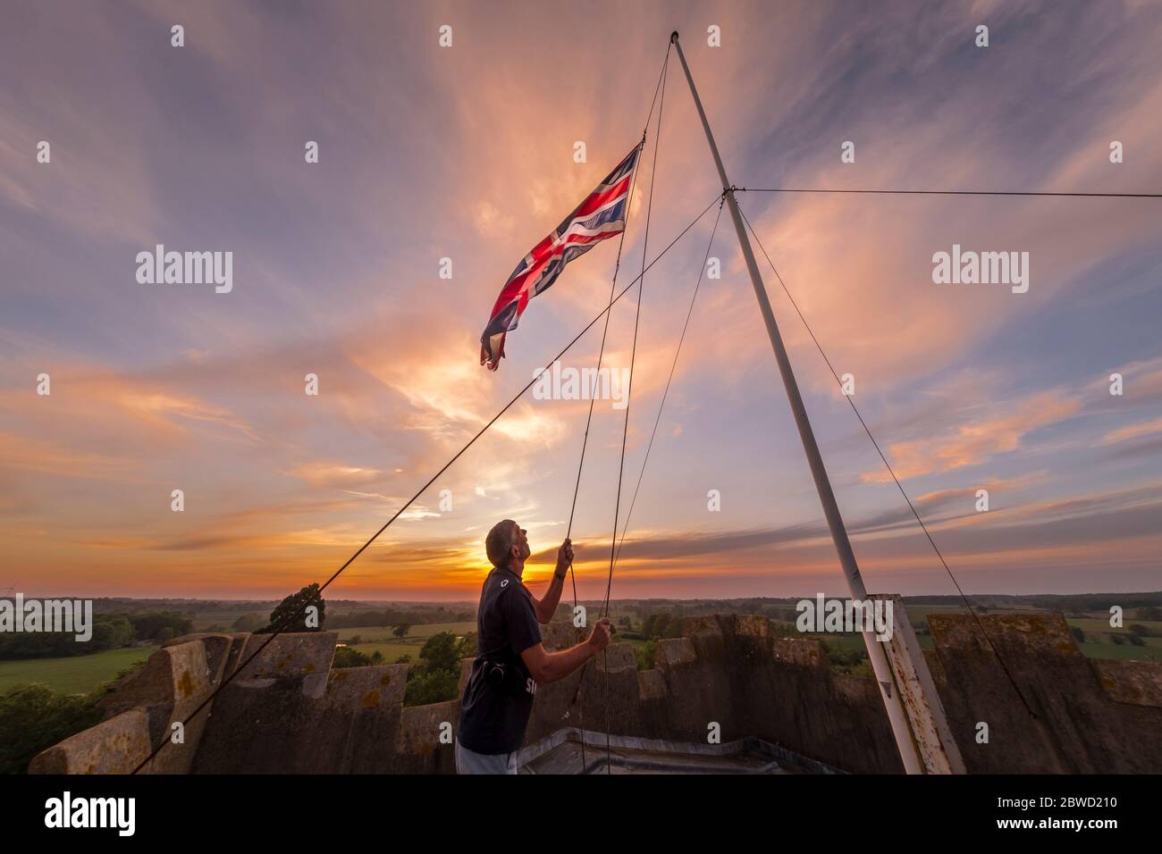 Abbassare la bandiera dell'Unione, nota anche come Union Jack al tramonto. Dopo le celebrazioni VE sul tetto della torre della chiesa, Hoxne, Suffolk, Regno Unito. Foto Stock