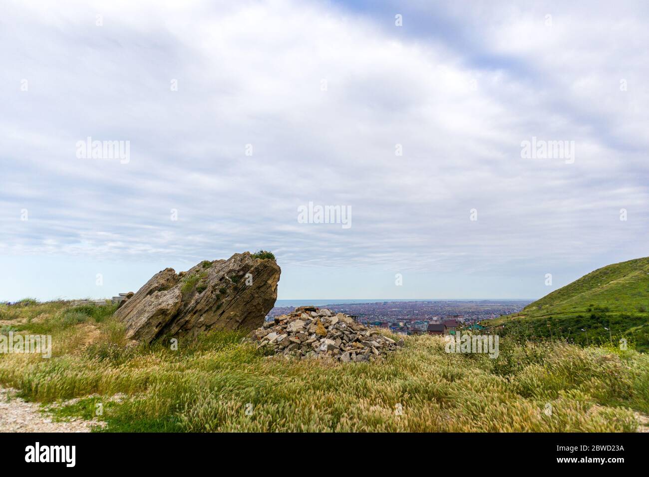 Grande pietra sulla montagna sopra la città con cielo nuvoloso sfondo. Foto Stock