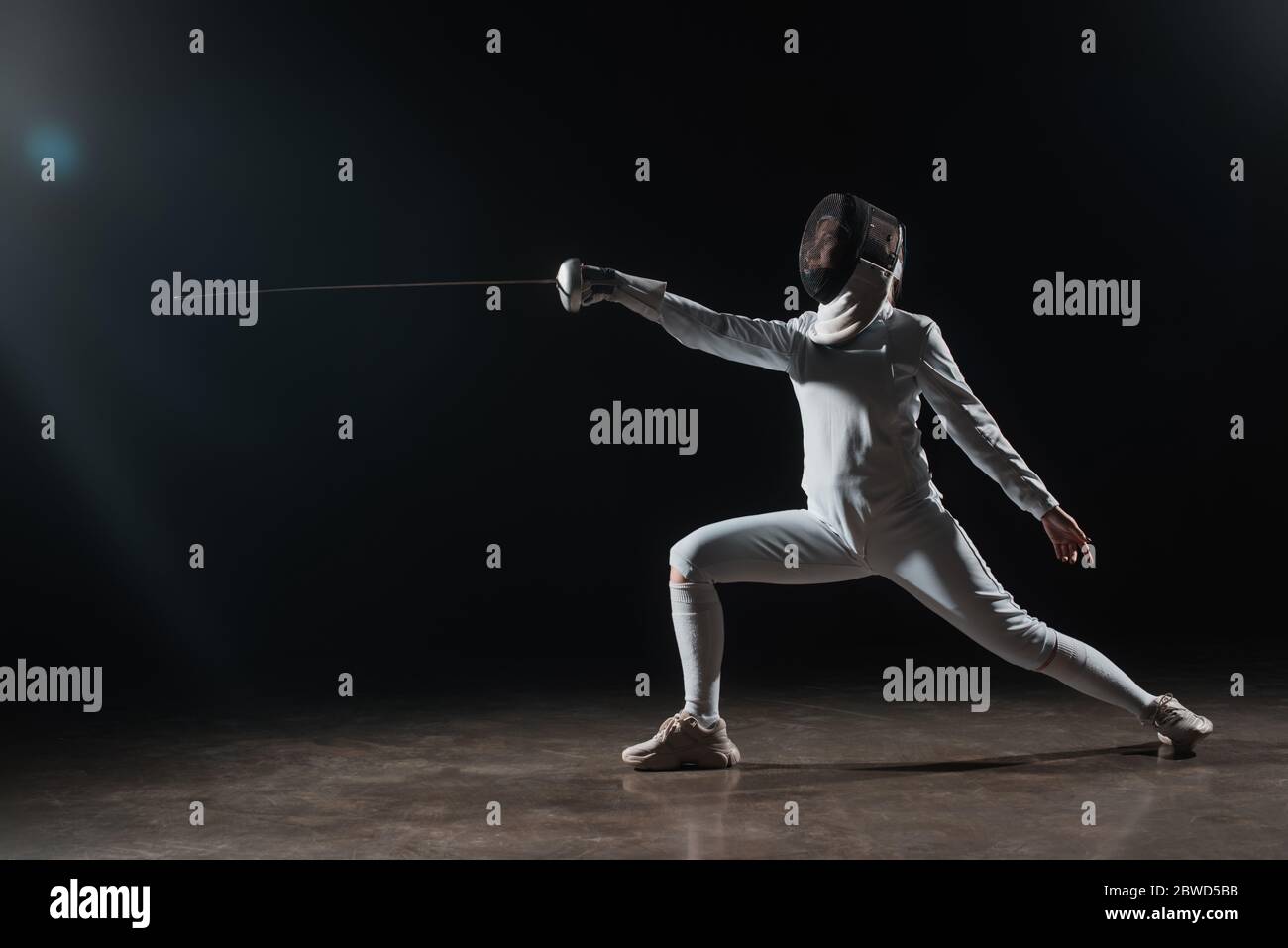 Fencer in scherma maschera facendo affondo mentre si allenano con più rapier su sfondo nero Foto Stock