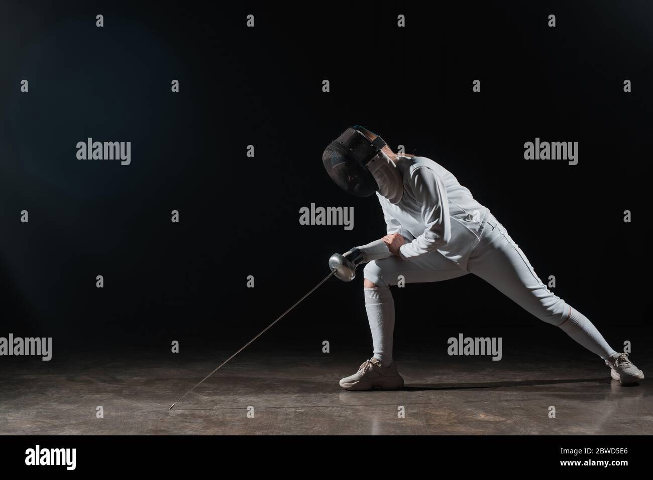 Fencer in maschera scherma e vestito che tiene la pinza e fa affondo su sfondo nero Foto Stock