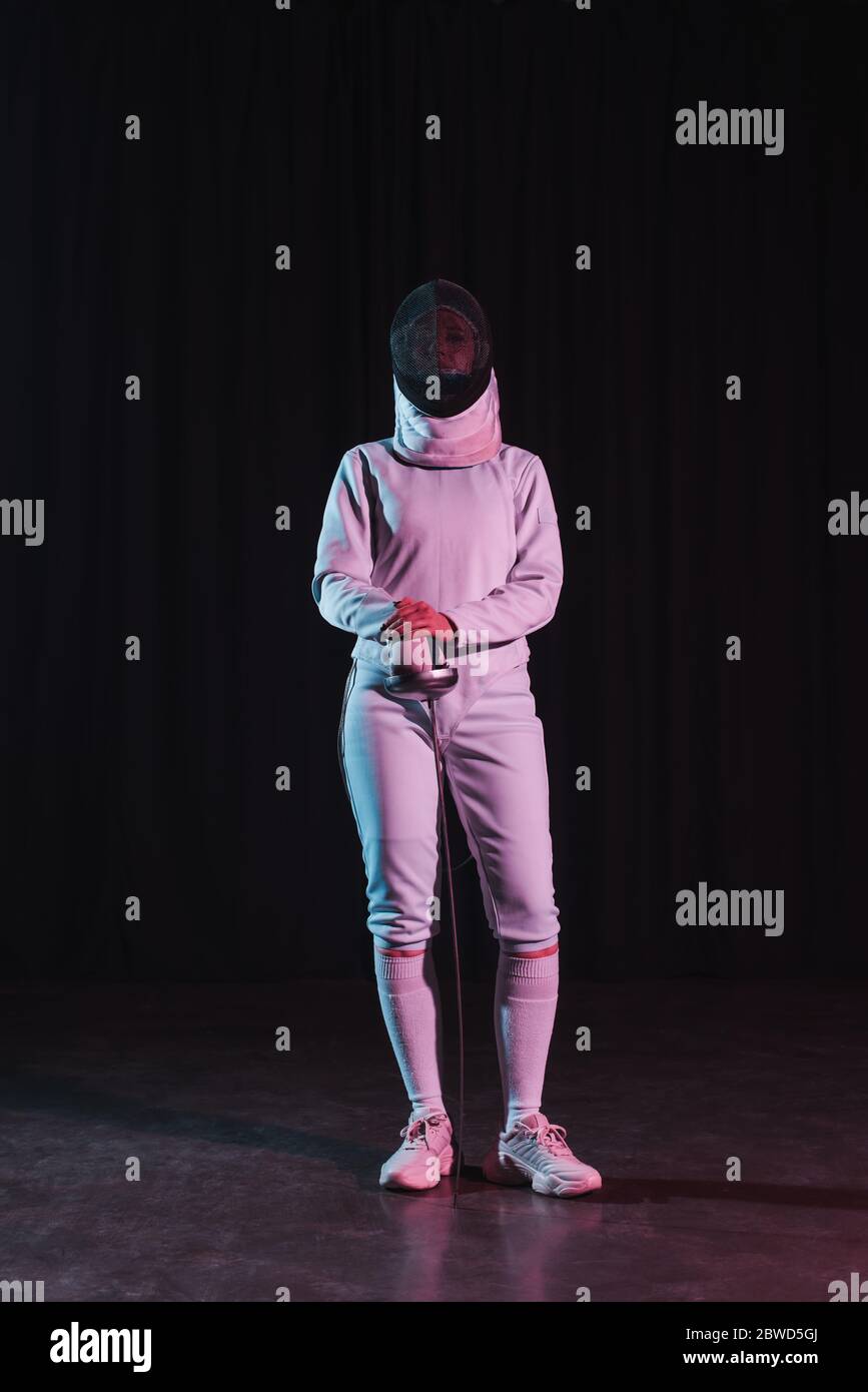 Fencer in tuta da scherma e maschera che tiene la pinza su sfondo nero Foto Stock