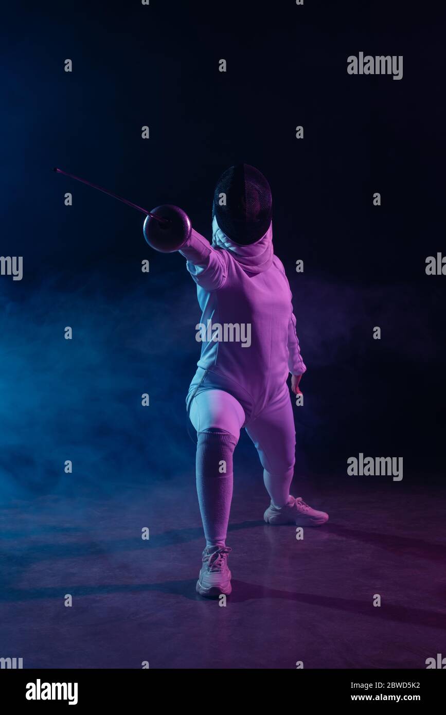 Fencer fare affondo mentre si allenano con una pinza su sfondo nero con fumo e illuminazione Foto Stock