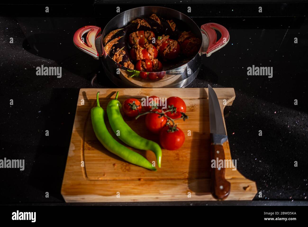 Vista dall'alto di peperoni verdi, tomatos e coltello su tagliere di legno per preparare kebab di melanzane turche, kebab di patlican con polpette Foto Stock