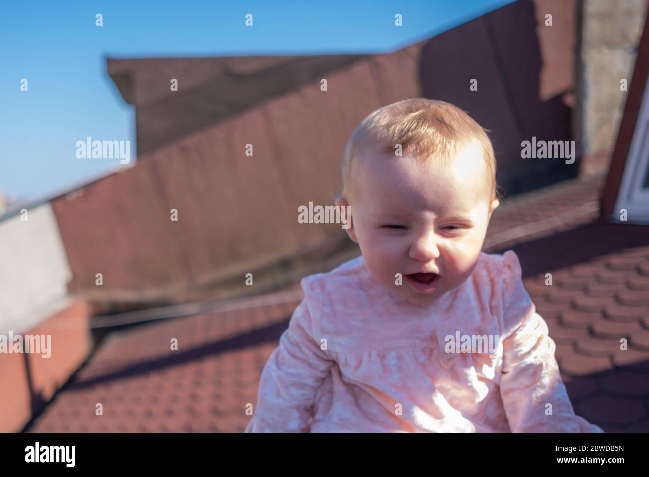 Primo piano di cute baby girl indossare adorabile vestito sul tetto, bolle di sapone galleggianti intorno, bambina cercando di prendere le bolle Foto Stock