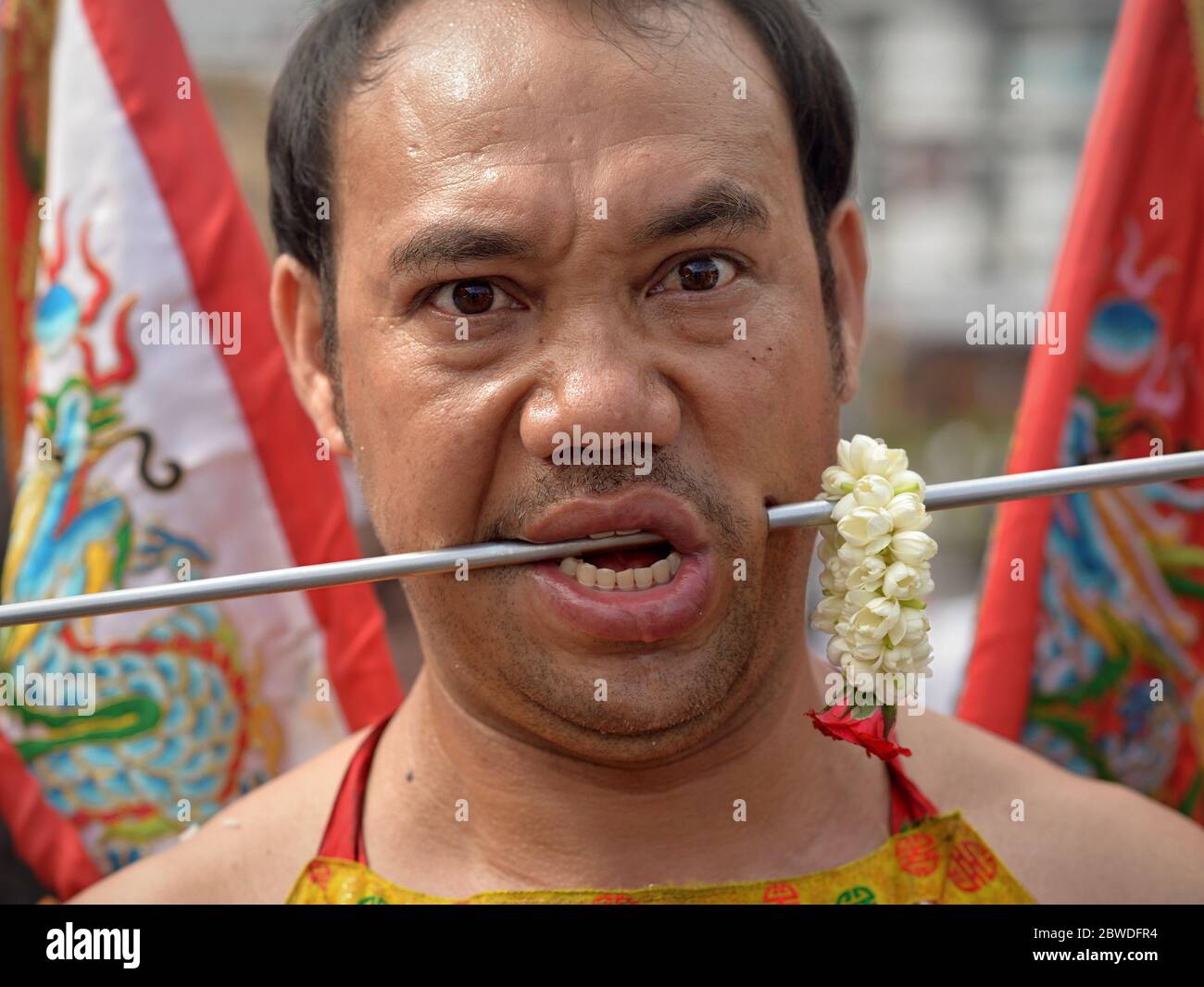 Il devoto taoista cinese tailandese pierces la sua guancia sinistra con un lungo perno di acciaio durante il Festival vegetariano di Phuket (Nine Emperor Gods Festival). Foto Stock