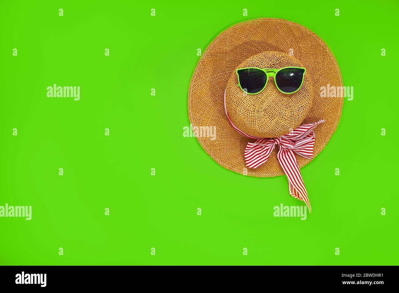 Accessori per la stagione balneare. Cappello di paglia e occhiali da sole isolati su sfondo verde. Vista dall'alto, disposizione piatta Foto Stock