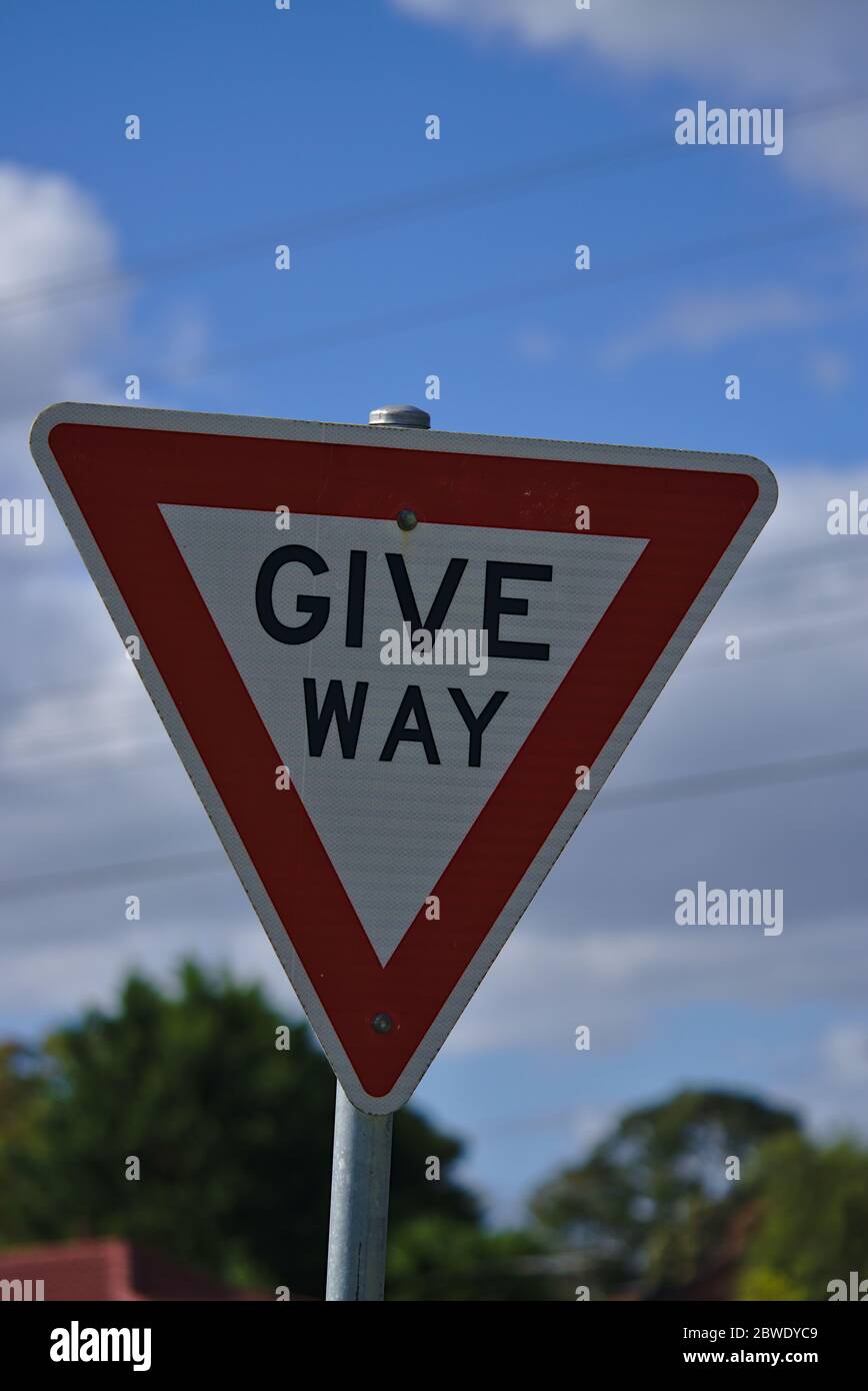 Vista ravvicinata del segno Give Way a forma di triangolo rosso e sfondo blu del cielo Foto Stock