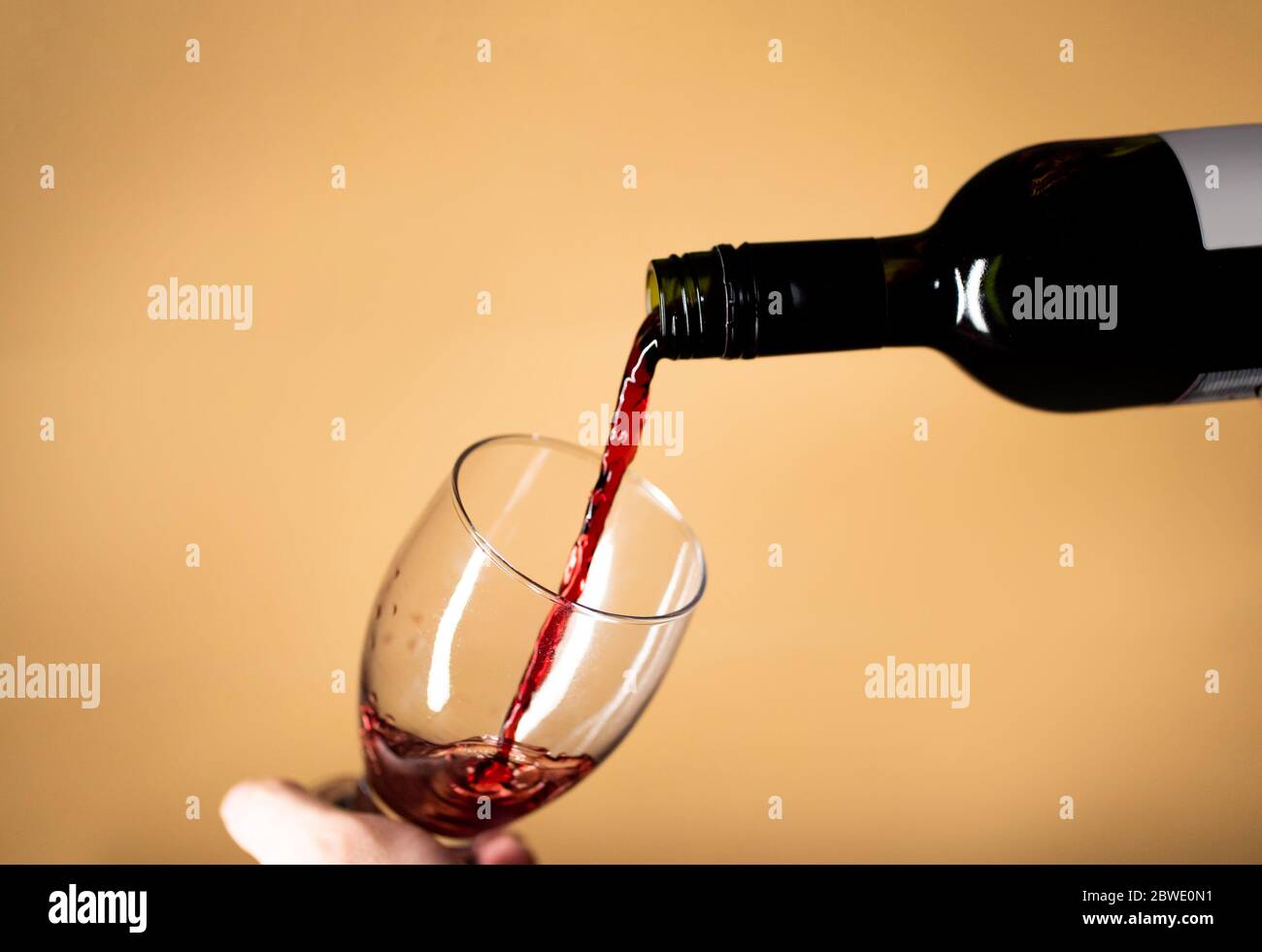 Serve un bicchiere di vino rosso che si spruzzi sul colore di fondo beige in vetro Foto Stock