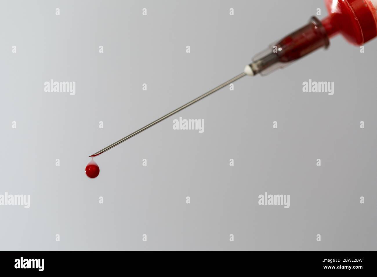 Siringa con un campione di sangue. Una goccia di sangue all'estremità dell'ago. Chimica del sangue. Analisi del sangue per virus. Foto Stock