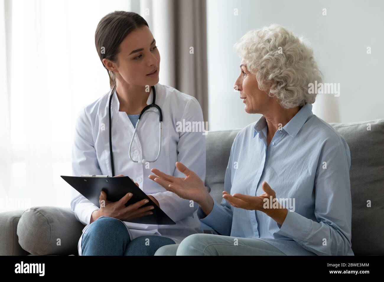 Donna anziana che parla di reclami per la salute a un giovane infermiere Foto Stock