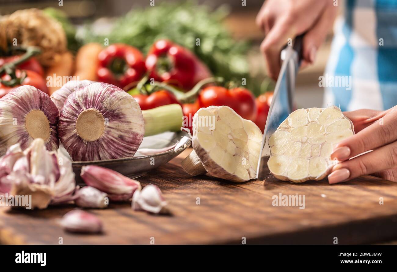 Dettaglio della testa dell'aglio tagliata a metà con aglio non sbucciato più fresco sul lato e varie verdure sullo sfondo Foto Stock