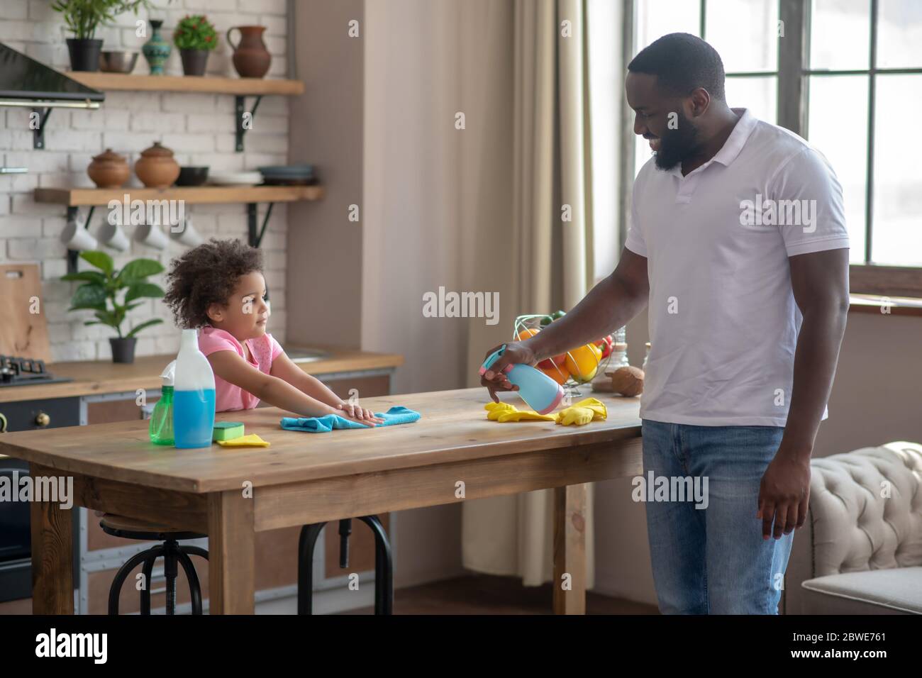 Disinfetta di spruzzatura dell'uomo alto afroamericano sulla superficie del tavolo Foto Stock