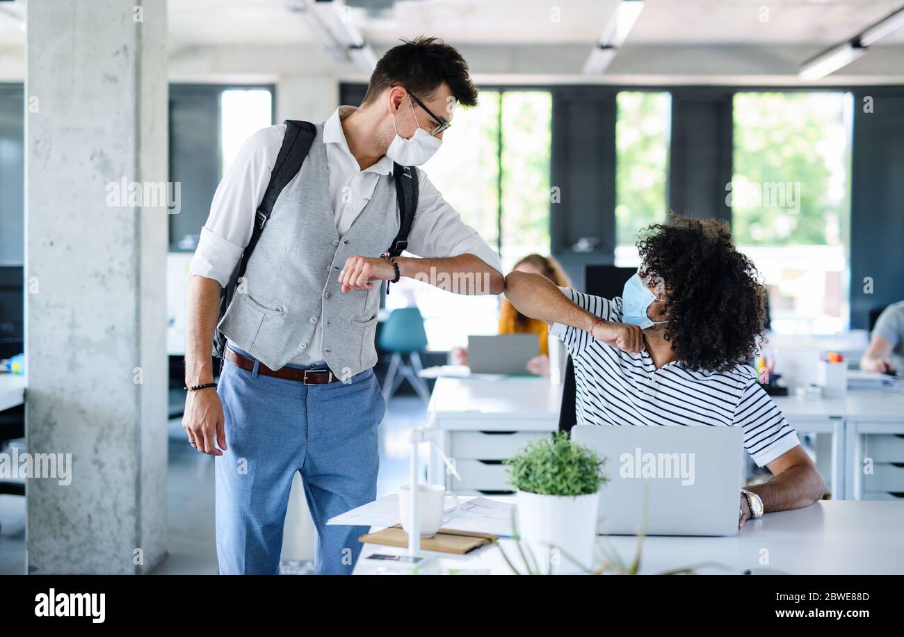 Giovani con maschere di fronte al lavoro in ufficio dopo blocco, saluto. Foto Stock