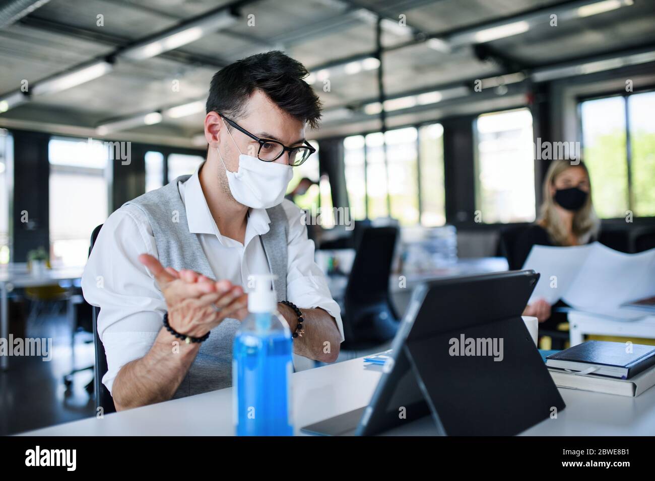 Giovani con maschere facciali al lavoro in ufficio dopo la chiusura, disinfezione delle mani. Foto Stock