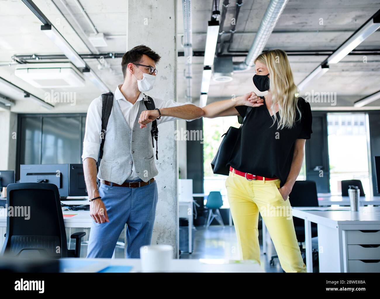 Giovani con maschere di fronte al lavoro in ufficio dopo blocco, saluto. Foto Stock