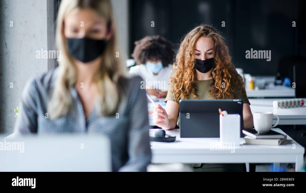 Giovani con maschere di fronte al lavoro o a scuola in ufficio dopo il blocco. Foto Stock