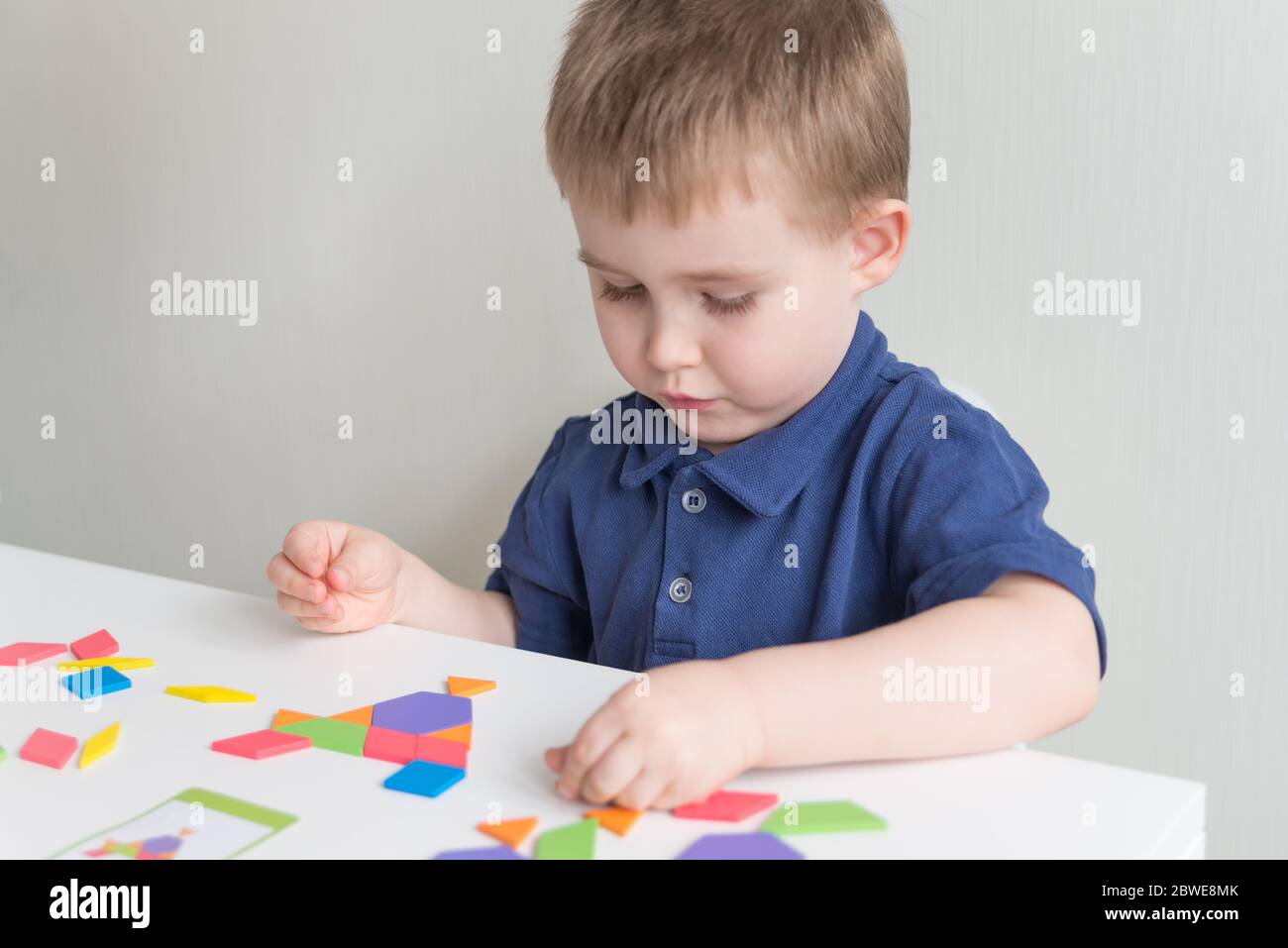 Il ragazzo carino gioca tangram di gioco di legno. Giochi creativi ed educativi sulla quarantena. Spazio di copia Foto Stock