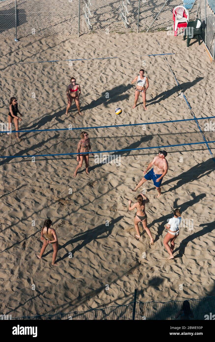 gruppo di giovani che giocano a beach volley, incorniciati dall'alto, con la luce bassa del sole che si inquadra in lunghe ombre Foto Stock