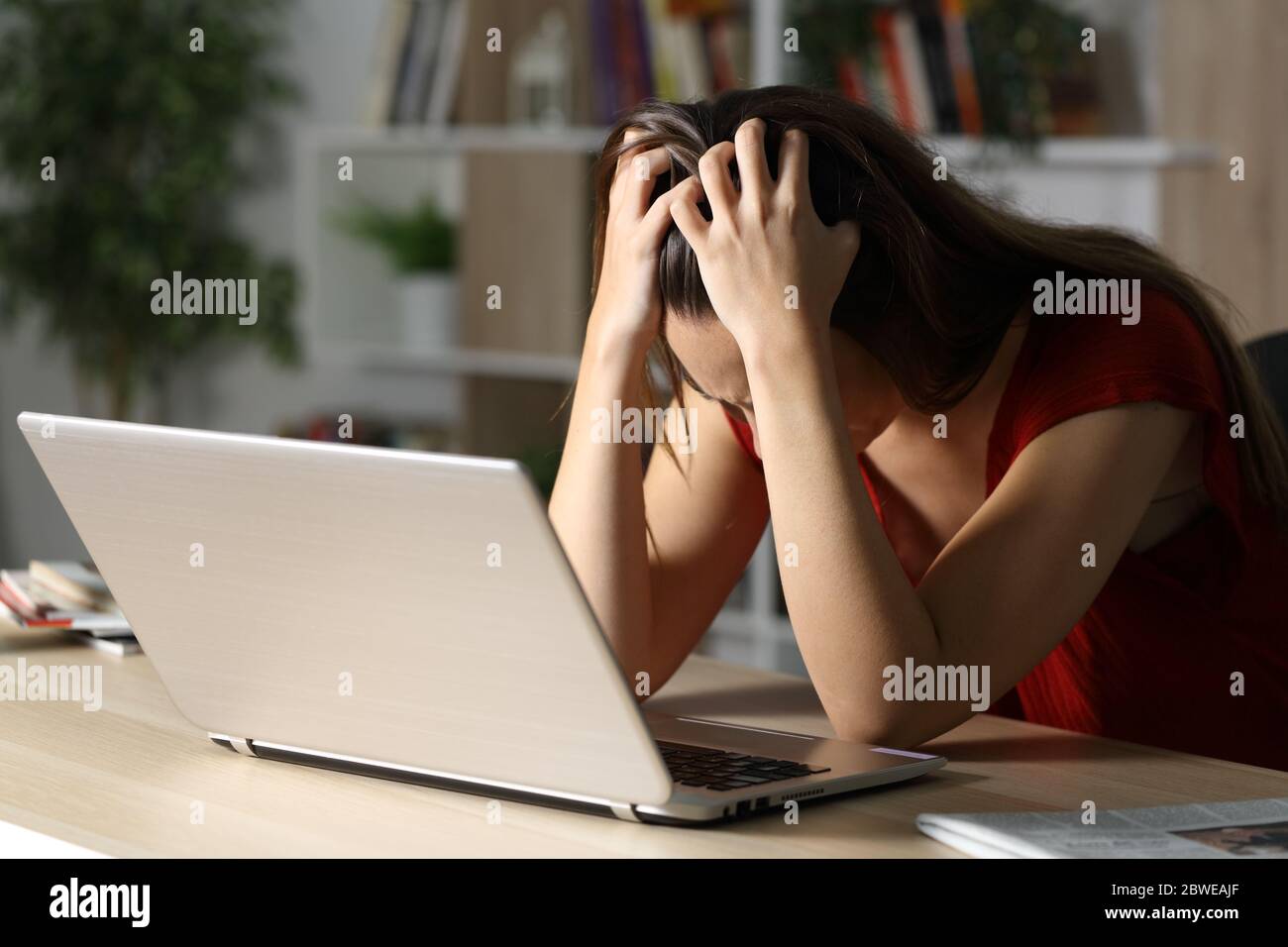 Triste donna con un computer portatile che si lamenta di essere seduta su una scrivania da sola di notte a casa Foto Stock