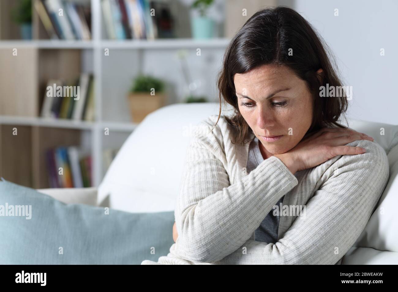 Triste penosa donna di mezza età che guarda giù depresed seduta sul divano nel soggiorno a casa Foto Stock
