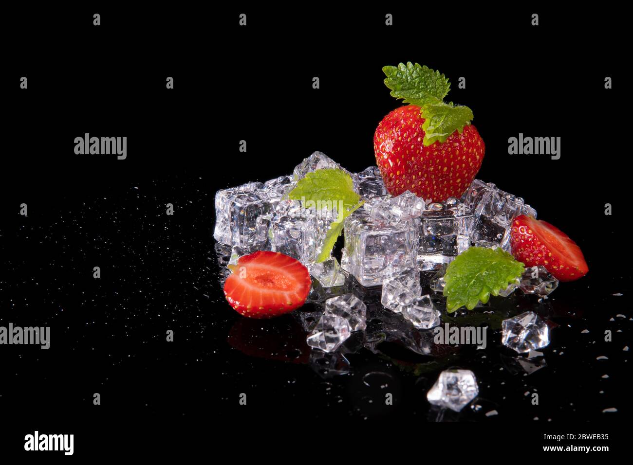 Fragole, foglie di menta e cubetti di ghiaccio su sfondo nero con riflessi Foto Stock