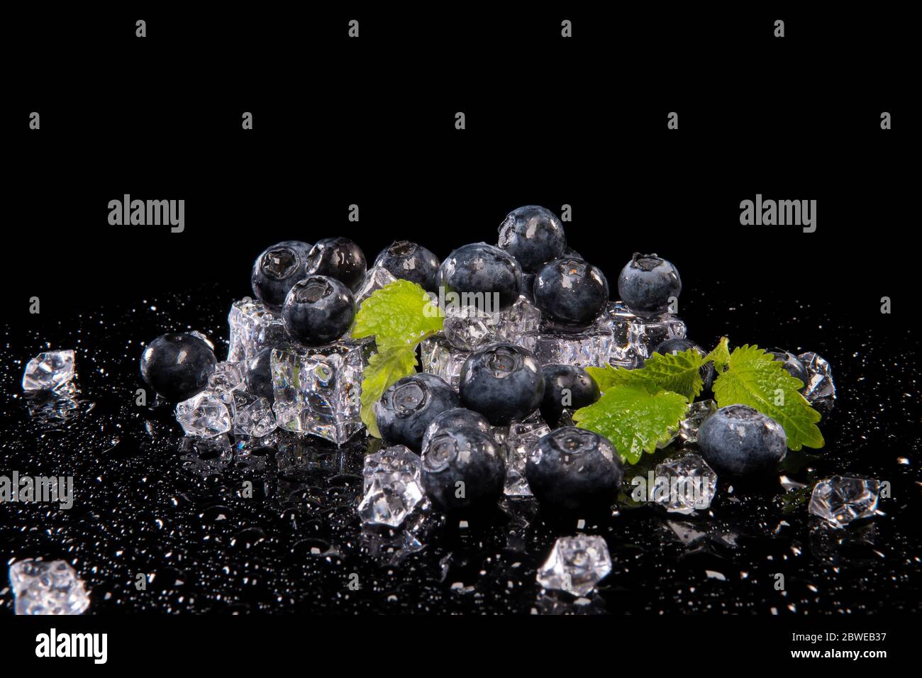 Mirtilli, foglie di menta e cubetti di ghiaccio su sfondo nero con riflessi Foto Stock