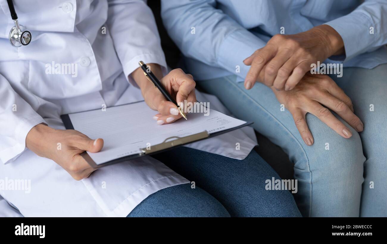 Vista di primo piano infermiere scrittura di informazioni personali ascolta pazienti anziani Foto Stock
