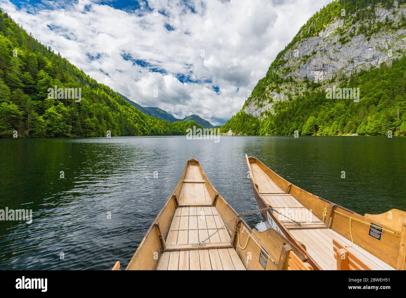 Splendida vista della tradizionale barca a remi in legno su Scenic. Il lago di montagna estivo passa la luce panoramica del mattino alle nuvole all'alba su alberi blu cielo verde Foto Stock