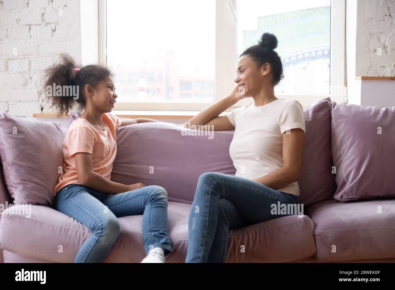 Madre e figlia africane che parlano seduto sul divano a casa Foto Stock