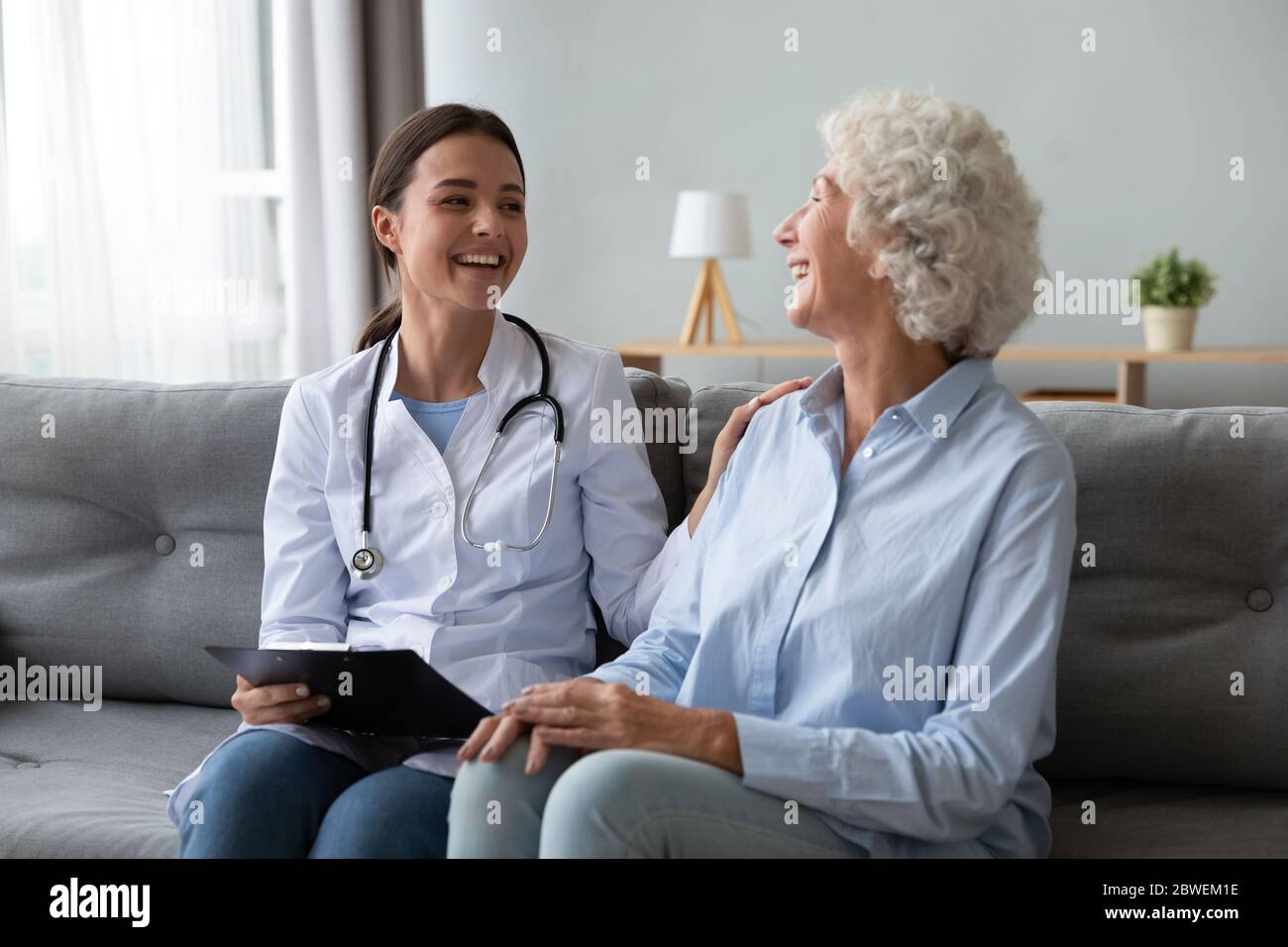 Infermiera amichevole che ride con la paziente anziana durante la visita di homecare Foto Stock