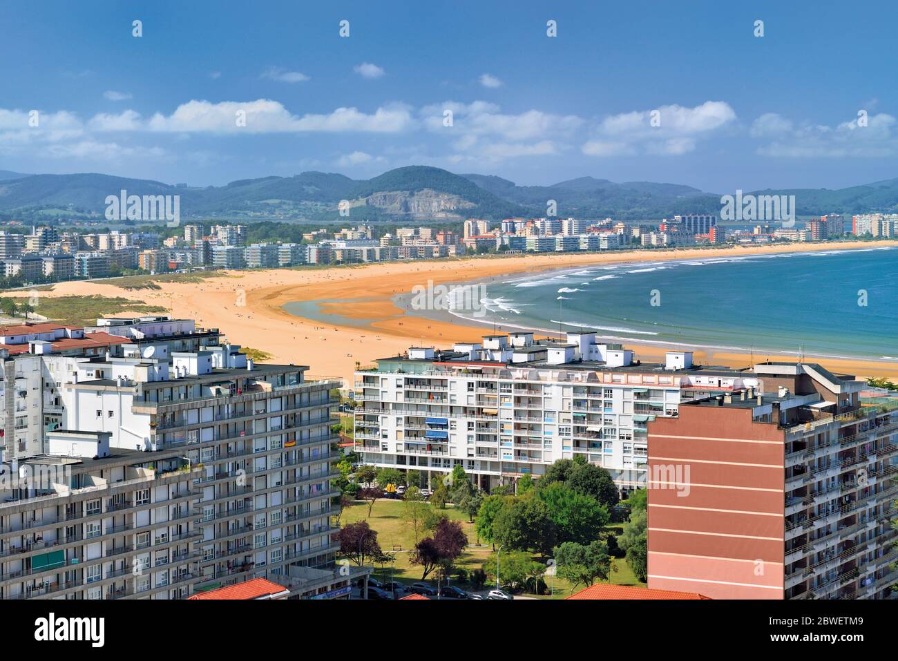 Vista sulla città con ampia spiaggia di sabbia e montagne verdi sullo sfondo Foto Stock