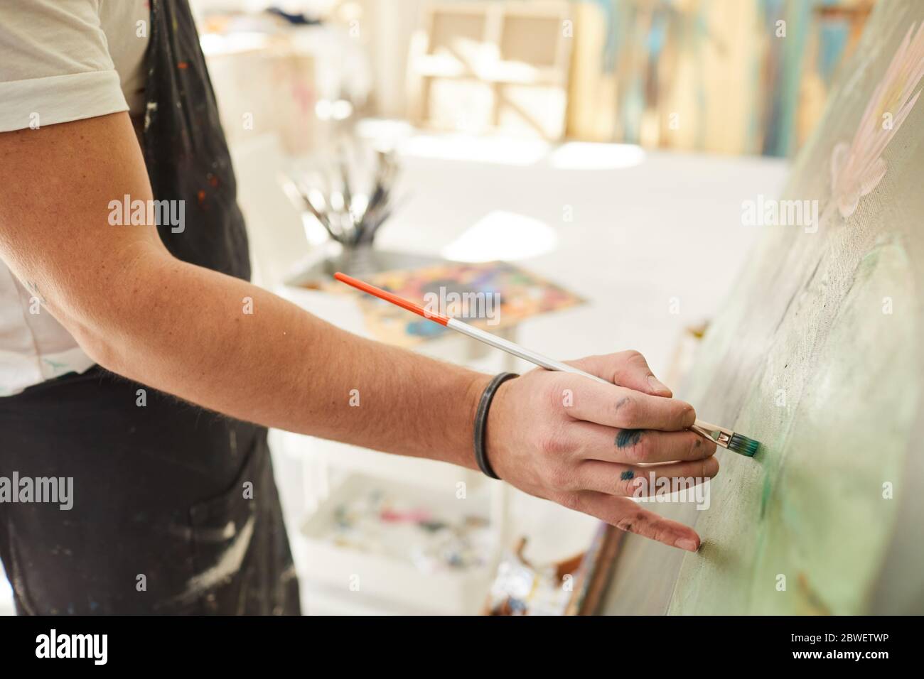 Primo piano di artista maschile irriconoscibile tenendo pennello e mettendo con attenzione i tratti di vernice mentre dipingono l'immagine su cavalletto, copia spazio Foto Stock