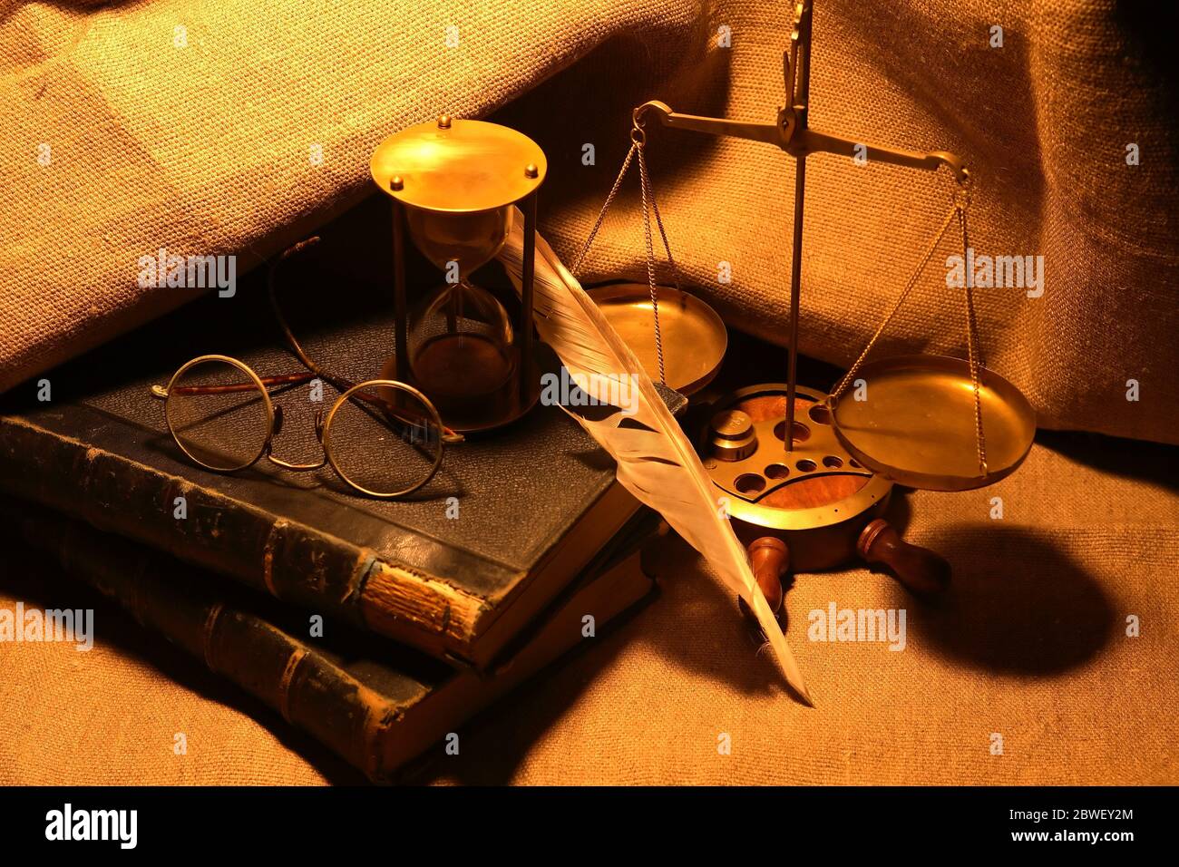 Vecchi libri e penna di quill vicino clessidra su sfondo di tela Foto Stock